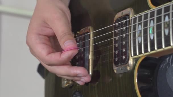 La personne frappe les cordes de la guitare électrique tenant un pic à la main, gros plan. Musicien pratique ou apprend une nouvelle mélodie. Concept de passe-temps et de divertissement — Video