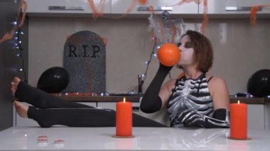 İskelet kostümlü ürkütücü makyajlı genç bir kadın Cadılar Bayramı partisi için balon şişiriyor. Gitmesine izin veriyor ve uçup gidiyor, sönüyor.