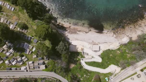 Cementerio con hermosas lápidas en la parte superior del acantilado cerca de la costa del Adriático en el casco antiguo de Ulcinj en Montenegro, vista superior, tiro con drones. Sendero aburrido conduce a la playa — Vídeos de Stock