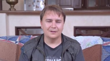 Deri ceketli genç adam kanepeye oturur ve hafifçe dans eder, başını öne doğru sallar. Olanlardan memnun değil, gözlerini devirip iç çekiyor.