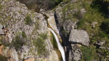 Kameralı insansız hava aracı kayalıklardan aşağı iniyor, kayaların arasından gürültülü bir şekilde su akıntısının durgun suya düştüğü yere. Ormandaki ya da milli parktaki eğlencelerin genel görünümü. Seyahat vlog 'u
