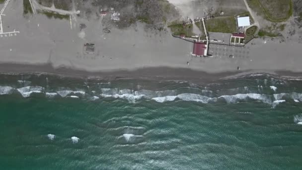 Drone con cámara vuela alto a lo largo de la costa arenosa, que es bañado por olas espumosas de mar Adriático turquesa oscuro, vista superior. Infraestructura del complejo en la playa desierta en la temporada baja — Vídeos de Stock