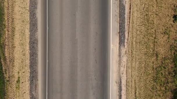 Drone con la cámara vuela sobre una carretera de asfalto, a lo largo de la cual los coches están pasando, y en los bordes de la carretera hay una tierra agrietada cubierta con hierba seca, vista superior — Vídeos de Stock