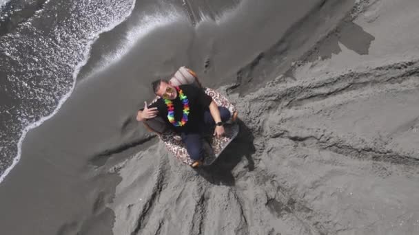 Cooler Typ mit Sonnenbrille und hawaiianischem Blumenstrauß um den Hals rappt und macht charakteristische Bewegungen mit den Händen, während er im alten Stuhl am Meer sitzt, Drohne dreht sich langsam herum, Draufsicht — Stockvideo