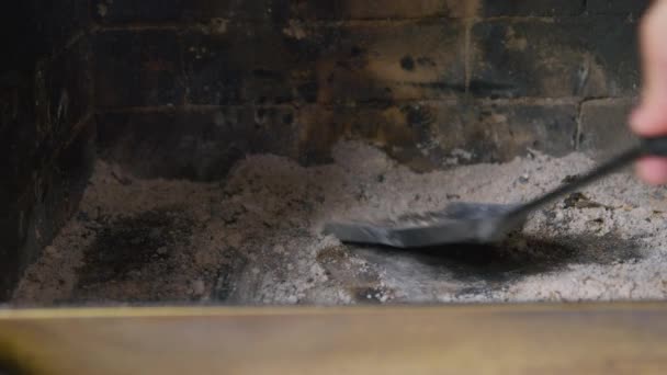 Człowiek używa starej żelaznej patelni, aby mieszać i zbierać popiół i popiół z drewna na opał po tym, jak spłonął, zbliżenie. Czyszczenie kominka po użyciu — Wideo stockowe