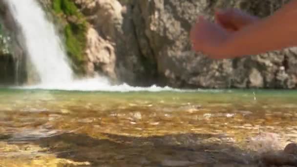 La persona toma agua potable en sus manos del río cristalino con cascada, para saciar la sed después de un largo paseo en la naturaleza o caminata en las montañas, o para lavarse la cara, de cerca — Vídeo de stock