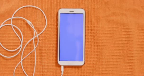 Phone with empty screen and earphones on orange fabric — Stock Video