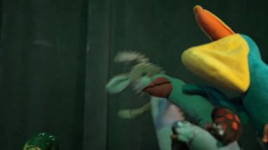 Birçok renkli pelüş oyuncak dans eder veya mor sahne ışıkları altında bir tiyatro veya disko sahnesindeki perdeye karşı gösteri yapar.