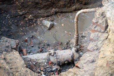 Hasarlı metal borular kısmen çamurlu suya batmış ve etrafı kırık tuğlalarla ve tamir altındaki kazılmış bir bölgede ıslak toprakla çevrili.