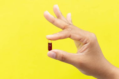 Sarı arka planda kapsül ya da hap tutan parmaklar yakın plan.