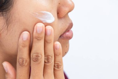 Kadının cilt bakımı için parmak uçlarıyla yanağa krem sürüşünün yakın çekimi. Sakin bir cilt bakımı anı ve günlük güzellik rutini sergiliyor..