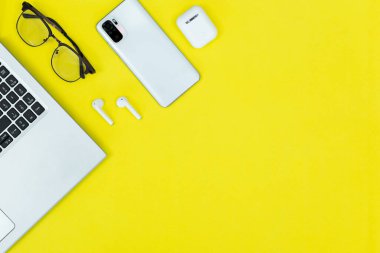 Düz konum Modern Teknoloji Masası Dizüstü, Akıllı Telefon, Gözlükler ve Kablosuz Kulaklıklar Sarı Arkaplanda. Ev ofisi, teknoloji yaşam tarzı ve verimlilik temaları için mükemmel..
