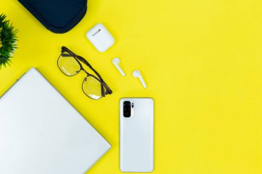 Dizüstü bilgisayarı, akıllı telefonu, kulaklığı ve ofis malzemelerini temiz bir masanın üzerine koyan modern minimalist çalışma alanının üst görüntüsü. Uzaktan çalışma, dijital verimlilik ve teknoloji kavramı.