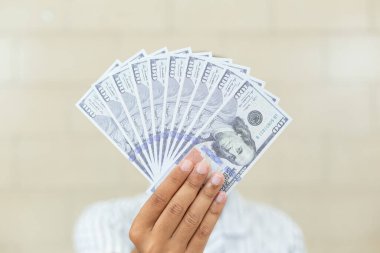 Yüz dolarlık banknotların yüzünü örten bir vantilatörle el ele tutuşmak. Zenginlik kavramı, finansal başarı, piyango talihlisi veya maaş günü.