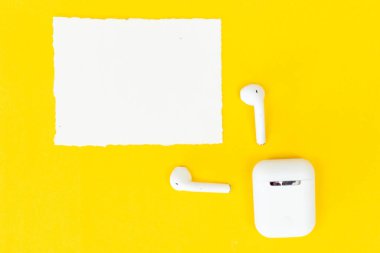 Müzik listesi veya podcast konsepti için sarı arkaplan üzerinde boş yırtık kağıt modeliyle düz kablosuz kulaklıklar yatıyordu