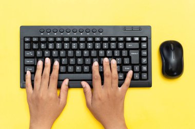 Siyah klavyede yazı yazan ellerin üst görüntüsü ve canlı sarı arka planda bir fare kullanımı. Veri girişi, ofis çalışması veya uzaktan üretkenlik kavramı