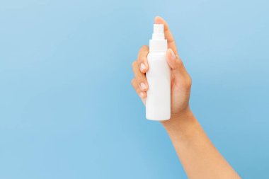 Temiz, açık mavi bir arka planda beyaz bir kozmetik sprey şişesinin maketini tutuyor. Minimalist hijyen veya kişisel bakım ürünü sunumu