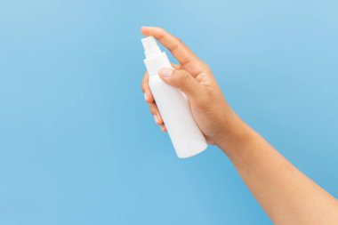 Temiz, açık mavi bir arka planda beyaz bir kozmetik sprey şişesinin maketini tutuyor. Minimalist hijyen veya kişisel bakım ürünü sunumu