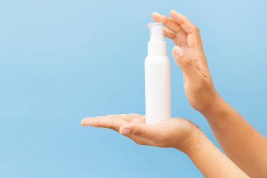 Temiz, açık mavi bir arka planda beyaz bir kozmetik sprey şişesinin maketini tutuyor. Minimalist hijyen veya kişisel bakım ürünü sunumu