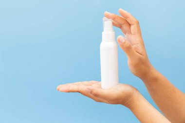 Temiz, açık mavi bir arka planda beyaz bir kozmetik sprey şişesinin maketini tutuyor. Minimalist hijyen veya kişisel bakım ürünü sunumu