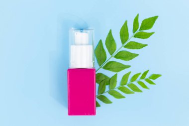 Saf mavi arka planda yeşil bitkisel yapraklı pembe kozmetik pompa şişesi, doğal saç bakımı veya organik güzellik ürünleri için mükemmel.