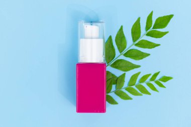 Saf mavi arka planda yeşil bitkisel yapraklı pembe kozmetik pompa şişesi, doğal saç bakımı veya organik güzellik ürünleri için mükemmel.