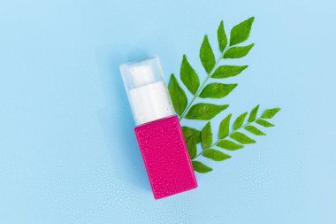 Saf mavi arka planda yeşil bitkisel yapraklı pembe kozmetik pompa şişesi, doğal saç bakımı veya organik güzellik ürünleri için mükemmel.