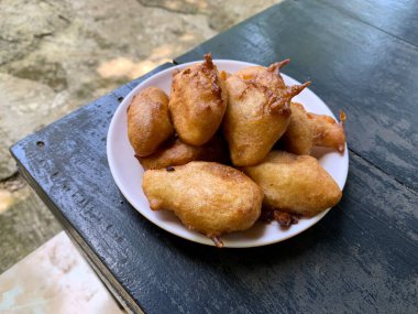 Pisang Goreng: Geleneksel Endonezya usulü kızarmış muzlu börekler, siyah ahşap bir masanın üzerinde beyaz bir tabakta servis ediliyor.
