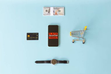 Kara Cuma 'nın en iyi görüntüsü akıllı telefon ekranında. Etrafı dolarlar, bir kredi kartı, bir minyatür alışveriş arabası ve açık mavi arka planda lüks bir erkek kol saati ile çevrili.