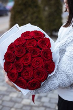 Açık havada bir kadın tarafından tutulan zarif beyaz ambalajlı güzel bir buket kırmızı gülün yakın çekimi. Sevgililer Günü, aşk ve kutlama için romantik hediye konsepti.