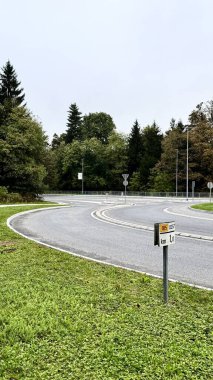 Uzun ağaçlar ve yemyeşil bitkilerle çevrili sık bir ormanda dolambaçlı bir yol kıvrılır. Asfalt yol yüzeyi, doğal manzarayla çelişiyor ve ağaçların arasında güzel bir manzara yaratıyor.