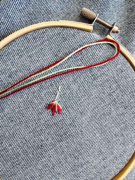 Embroidered flowers on fragment of blue denim jeans texture.