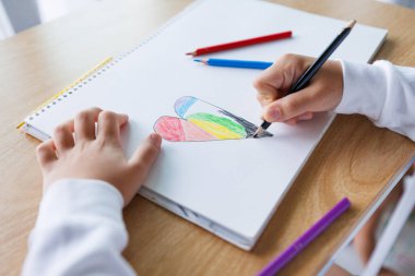 Çocukların kalp şeklini beyaz kağıda renkli kalemlerle boyamaları, yaratıcı çocukların sanat faaliyetleri, evde veya okulda eğitim ve öğrenme, çocukluk yaratıcılığı ve hayal gücü kavramları.