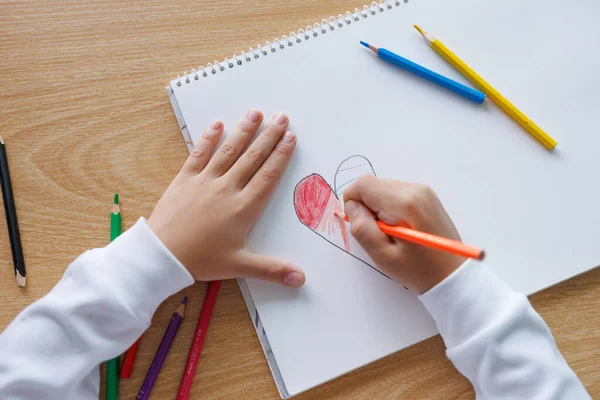 Kırmızı bir kalbi beyaz defter kağıdına renkli kalemlerle çizmek ve boyamak, çocuk sanatı ve öğrenme aktivitesi, çocuk yaratıcılığı, aşk ve eğitim kavramı, kapalı alanda doğal gün ışığı fotoğrafı.