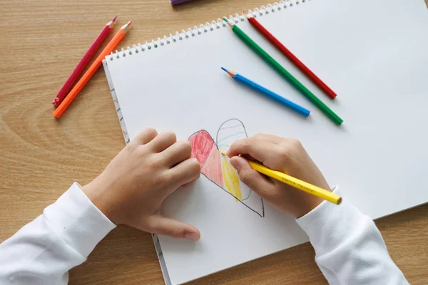 Gökkuşağı kalbini beyaz defter kağıdına renkli kalemlerle boyamak, çocuk sanatı ve öğrenme aktivitesi, çocuk yaratıcılığı, çizim ve eğitim konsepti, el yapımı aşk sembolü, doğal gün ışığı fotoğrafı.