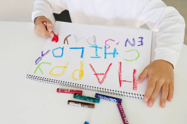 Kid creating bright crayon artwork on paper, rainbow colors, children creativity and early learning, art class concept