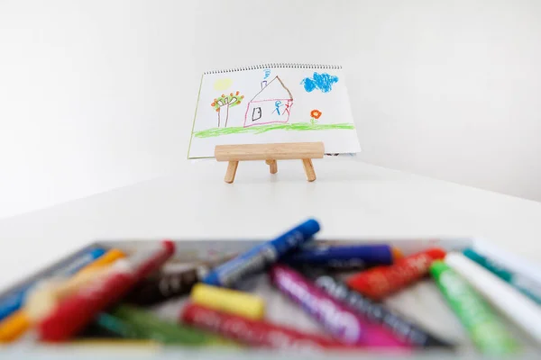 Child drawing displayed on an easel with colorful markers in the foreground. A bright minimalist room creates a creative and cozy atmosphere. Perfect for themes of childhood and education.