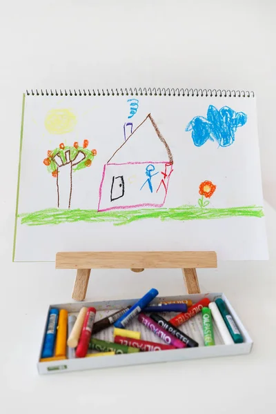 House drawing on an easel in a kids creative space with blurred markers in the foreground. Concept of art learning imagination and early childhood creativity.