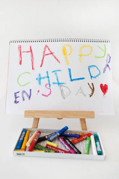 Colorful Happy Child Day drawing on a wooden easel with scattered crayons. Bright handmade art for children creativity theme, education, school projects and holiday celebration concepts.