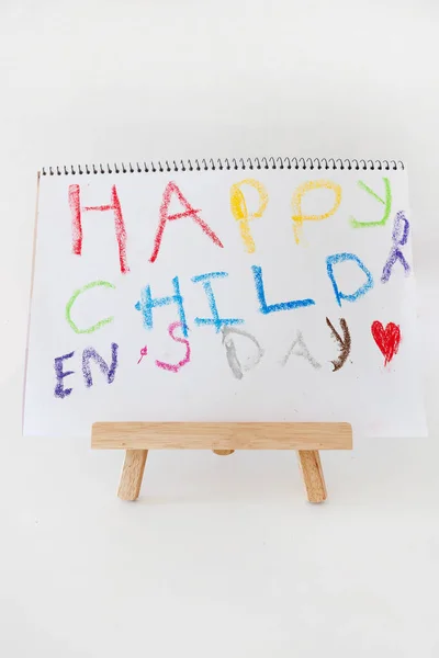 Colorful Happy Children Day drawing on a small wooden easel with oil pastels. Creative kids art concept, education and childhood celebration theme in bright colors.