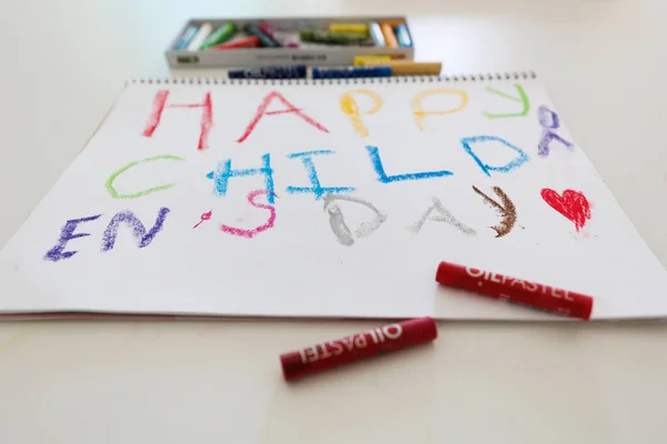 Colorful kids drawing with oil pastels spelling Happy Child Day on white paper. Creative child artwork, education, art supplies, holiday celebration, preschool activity.