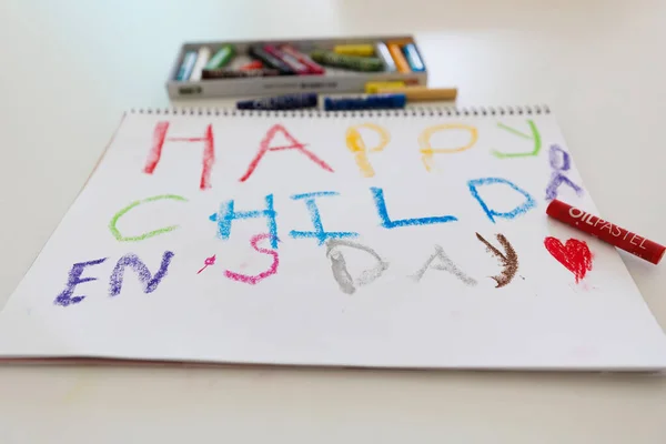 Happy Child Day message drawn with colorful oil pastels on sketchbook paper. Kids art project, creative learning, bright crayons, childhood celebration concept.