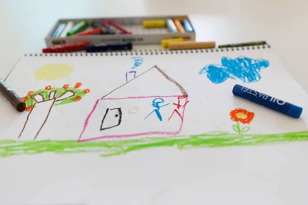 Child creative crayon drawing with a house, tree, sun and sky. Colorful kids artwork made with oil pastels on white paper. Perfect for themes of education, childhood, creativity and learning.