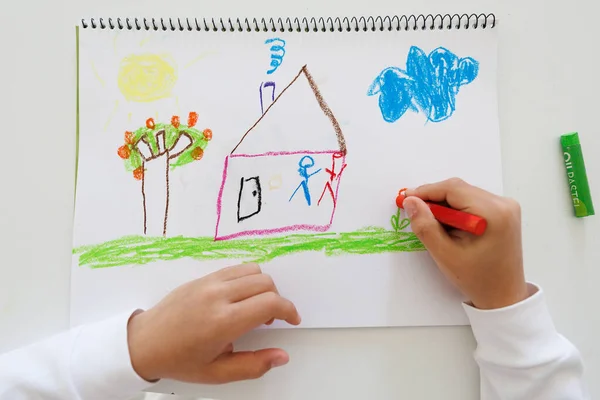 Close up of a child hands drawing a house and nature scene with colorful oil pastels. Great for themes of creativity, learning, early development and art education.