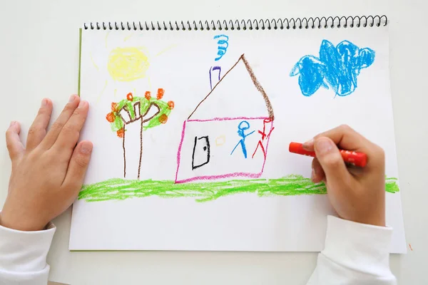 Child hands creating a playful pastel drawing of a house, tree and sky on sketchbook paper. Perfect concept for childhood creativity, imagination and art classes.