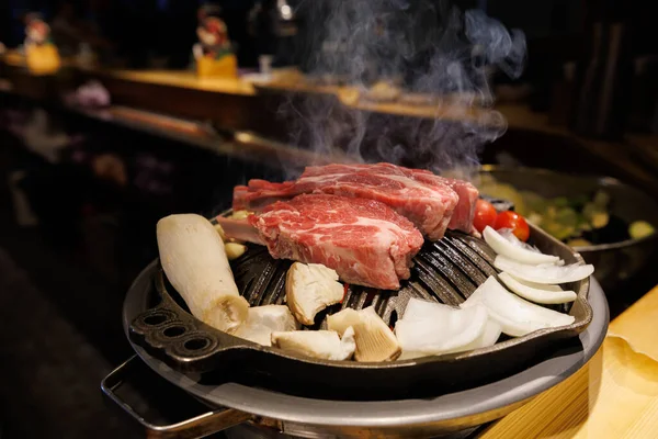 Korean BBQ beef grilling on a hot metal grill with mushrooms and onions in a restaurant setting. Traditional Asian barbecue food with steam and warm lighting.