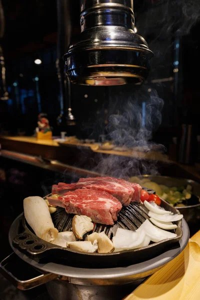 Close-up of fresh beef slices cooking on a Korean barbecue grill, surrounded by vegetables. Popular Asian cuisine, authentic restaurant dining experience.