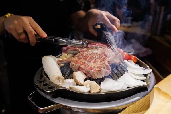 Hot Korean BBQ grill with beef steak and vegetables cooking in a cozy restaurant interior. Asian food culture and dining lifestyle.