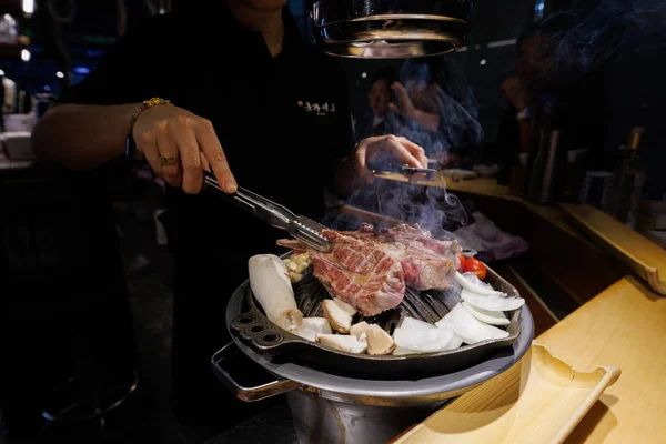 Close-up of human hands preparing Korean barbecue beef on a tabletop grill using scissors. Authentic Asian food culture and restaurant dining concept.