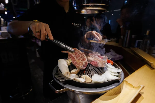 Traditional Korean BBQ scene with hands slicing grilled beef meat on a smoking grill. Popular Asian cuisine and social dining experience.